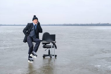 Takım elbiseli ve patenli gülümseyen işadamı donmuş göldeki masada oturuyor.