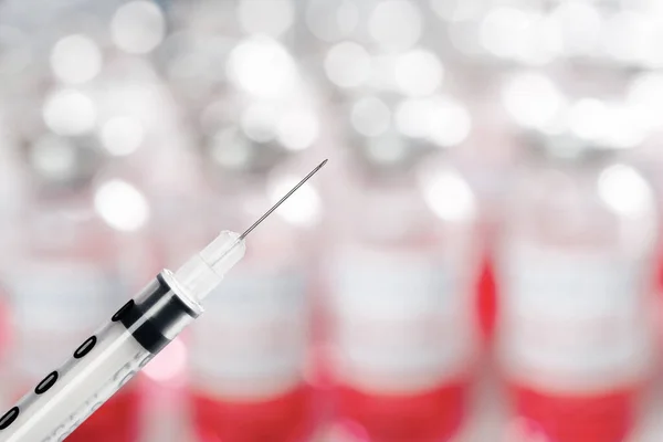 Igła strzykawki z bliska na niewyraźne fiolki szczepionki do walki z produktem Covid-19 — Zdjęcie stockowe