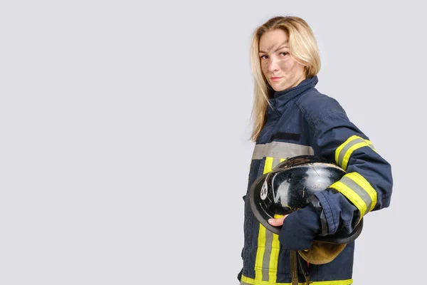 Mujer con la cara sucia en uniforme de bombero sostiene hardhat en la mano —  Fotos de Stock