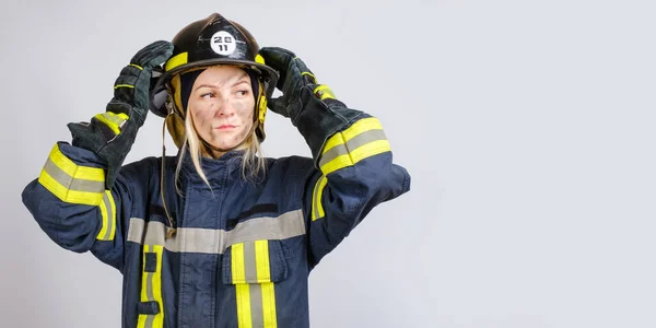 Joven valiente mujer en uniforme de bombero pone hardhat en su cabeza —  Fotos de Stock