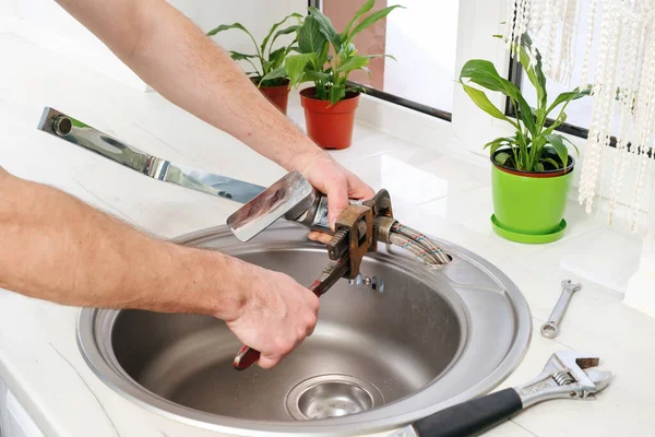 Plumber hands removes the old faucet from the sink with an adjustable wrench