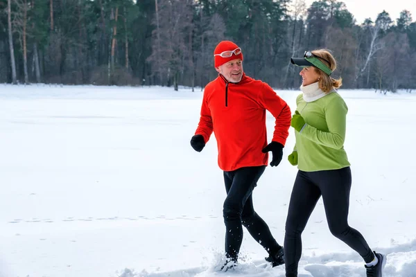 Sorrindo casal sênior jogging no parque de inverno nevado. — Fotografia de Stock