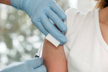 Doktor elleri hastanın omzunda aşı yapıyor. 