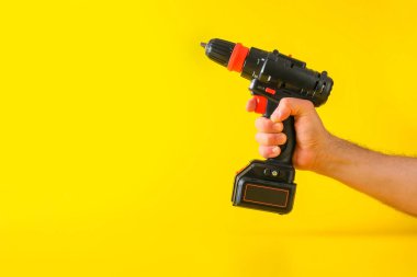 Sarı zemin üzerinde kablosuz tornavida ve kırpılmış erkek eli.