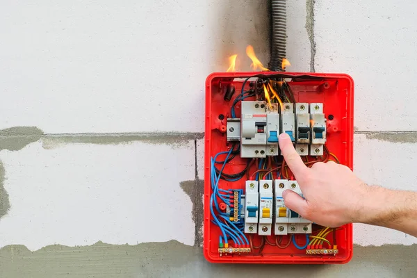 Male hand turns off burning switchboard from overload or short circuit on wall