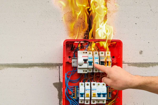 Male hand turns off burning switchboard from overload or short circuit on wall
