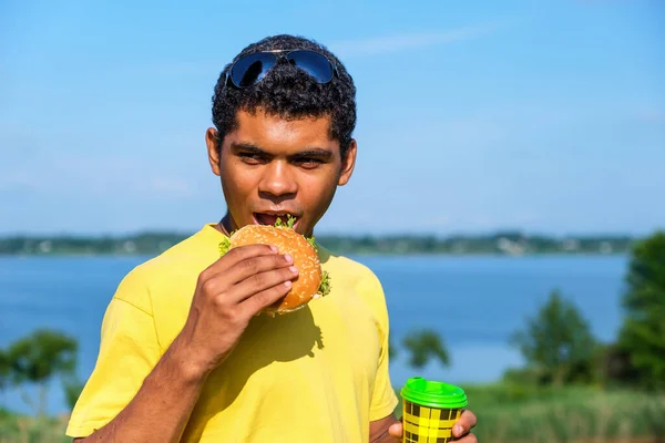 夏にはハンバーガーとコーヒーの屋外の味を楽しむ空腹のアフリカ系アメリカ人男性 ジャンクフードへの愛の概念 — ストック写真