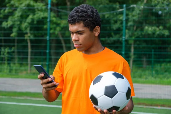 Portrét Mladého Usmívajícího Afroamerického Muže Držícího Fotbalový Míč Používajícího Smartphone — Stock fotografie