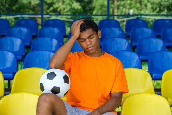 Brazilec s fotbalovým míčem sedí na prázdném fotbalovém tribuně — Stock fotografie