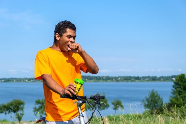 Genç adam kahve içiyor ve nehir boyunca bisiklet sürerken esniyor.
