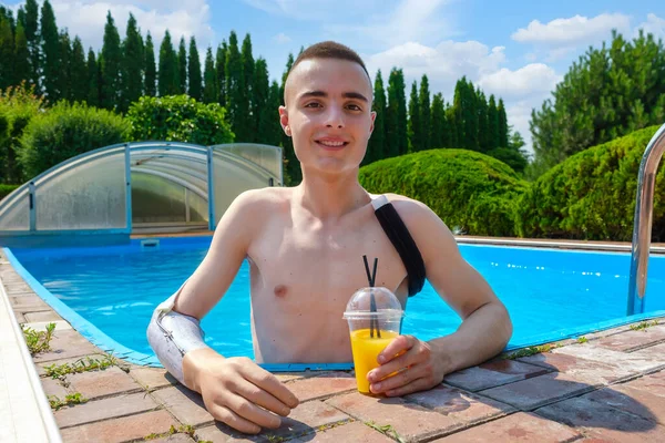 Uomo con braccio amputato e protesi beve un cocktail in piscina — Foto Stock