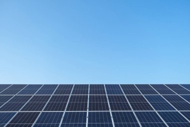 Mavi gökyüzünün altındaki bir güneş çiftliğinde sıra sıra güneş panelleri..