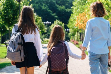 Okul üniformalı iki kız, anneleriyle birlikte okula yürüyorlar. 