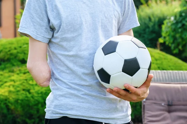 Homem com braço amputado segura pé na bola de futebol enquanto está no gramado — Fotografia de Stock