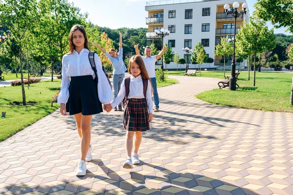 Δύο αδελφές κρατιούνται από το χέρι και πηγαίνουν σχολείο ενώ οι γονείς τους χαίρονται. — Φωτογραφία Αρχείου