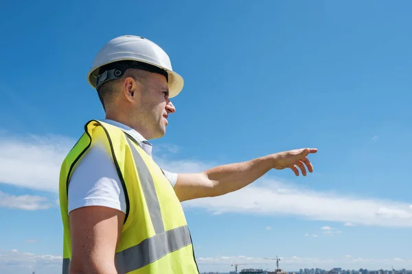 Budowniczy w białym hełmie pokazuje z ręką na placu budowy — Zdjęcie stockowe