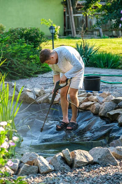 Człowiek czyści dno stawu ogrodowego myjką wysokociśnieniową z błota i osadu. — Zdjęcie stockowe