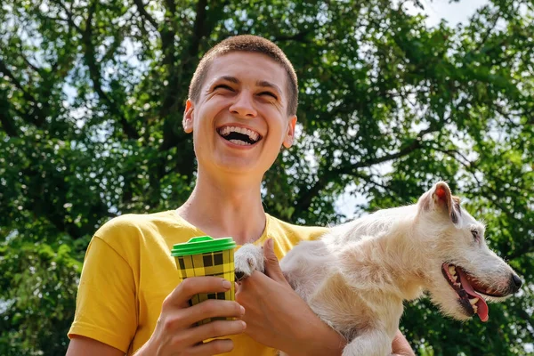 Mężczyzna trzyma psa Jack Russell i pije kawę z jednorazowego kubka na świeżym powietrzu — Zdjęcie stockowe