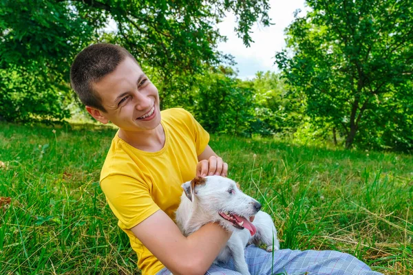 Homem senta-se na grama e traços cão Jack Russell terrier no parque de verão — Fotografia de Stock