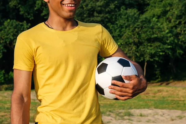Mladý usměvavý brazilský muž drží míč před hraním na travnaté písečné pláži — Stock fotografie