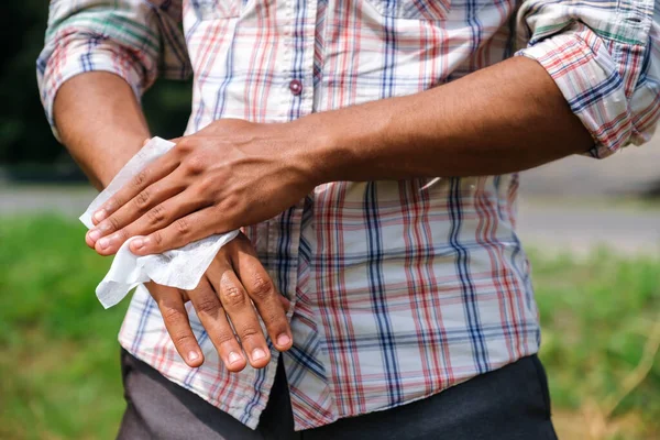 Man disinfecting his hands using wet wipe closeup outdoors to prevent infection