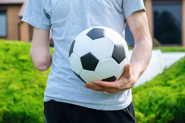 Muž s amputovanou paží drží nohu na fotbalovém míči, zatímco stojí na trávníku — Stock fotografie