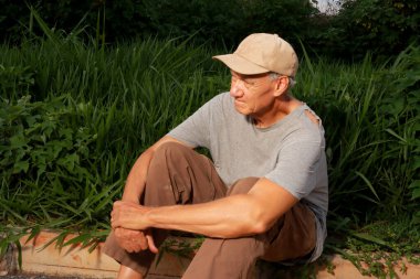 Yaşlı evsiz adam kaldırımda oturuyor ve başka tarafa bakıyor ve yalnız. 