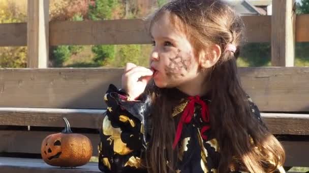 Dziewczyna w stroju czarownicy i czarny kapelusz na głowie z czarnym makijażem Halloween, zombie jedzące słodycze dżem robaki na uroczystości Halloween — Wideo stockowe