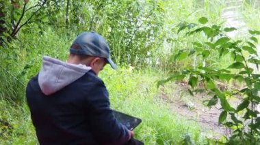 Sevimli Çocuk Tablet PC ile oynuyor. Arka planda ormanlık alan var. Bilgisayar Oyunu Bağımlılığı konsepti yakınında.