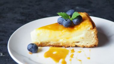 Lezzetli bir cheesecake dilimi ve siyah bir masada meyve..