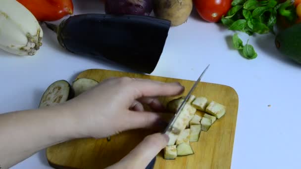 Mão feminina com faca corta berinjela a bordo na cozinha. Cozinhar vegetais. fazer um guisado vegetal ou salada. vegetarianismo, dieta, baixas calorias, nutrição adequada — Vídeo de Stock