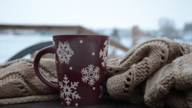 Kış ormanlarının arka planında kar taneleri desenli kırmızı ya da bordo bardak. Kar yağıyor. Yeni yıl. Noel zamanı. Bir kış şehrinin arka planında, pencerenin kenarında sıcak bir bardak..