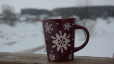 Kış ormanlarının arka planında kar taneleri desenli kırmızı ya da bordo bardak. Kar yağıyor. Yeni yıl. Noel zamanı. Bir kış şehrinin arka planında, pencerenin kenarında sıcak bir bardak..