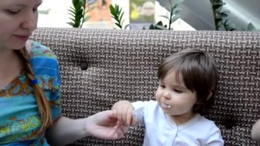 Toddler eat crying at lunch time sitting in a highchair in the living room at home. Mom feeds the baby girl in the cafe with healthy food. porridge, cottage cheese, yogurt spoon