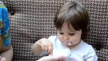 Toddler eat crying at lunch time sitting in a highchair in the living room at home. Mom feeds the baby girl in the cafe with healthy food. porridge, cottage cheese, yogurt spoon