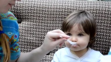 Toddler eat crying at lunch time sitting in a highchair in the living room at home. Mom feeds the baby girl in the cafe with healthy food. porridge, cottage cheese, yogurt spoon