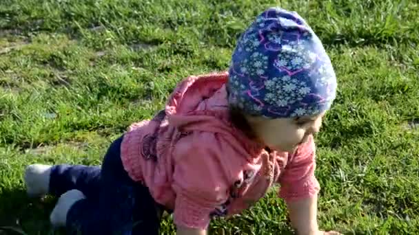 Leende söt lekfull liten flicka står på grönt gräs. Flicka småbarn promenader runt sjön lär sig att gå. solig speing eller sommardag — Stockvideo