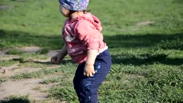 Sonriendo linda niña juguetona está de pie sobre hierba verde. niña pequeño camina alrededor del lago aprende a caminar. soleado sping o día de verano — Vídeos de Stock