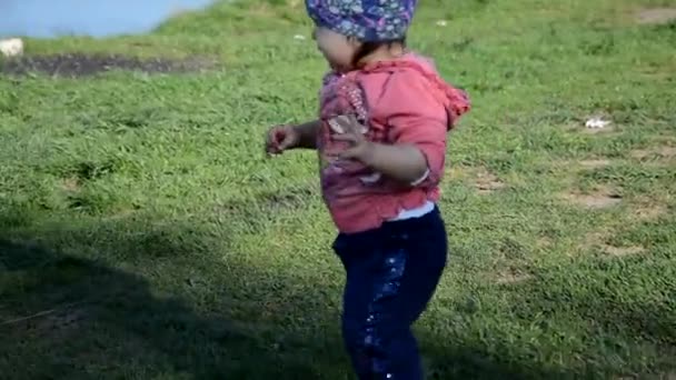 Sorrindo bonito brincalhão menina está de pé na grama verde. menina criança caminha ao redor do lago aprende a andar. sping ensolarado ou dia de verão — Vídeo de Stock