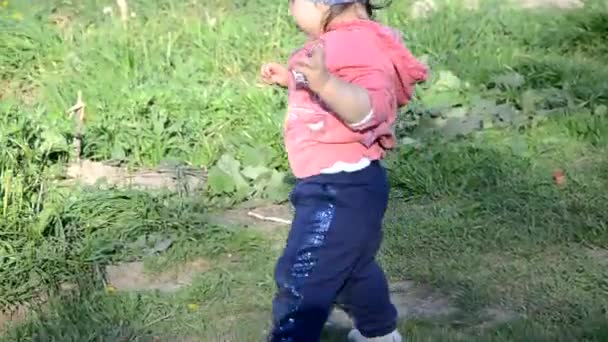 Sonriendo linda niña juguetona está de pie sobre hierba verde. niña pequeño camina alrededor del lago aprende a caminar. soleado sping o día de verano — Vídeos de Stock