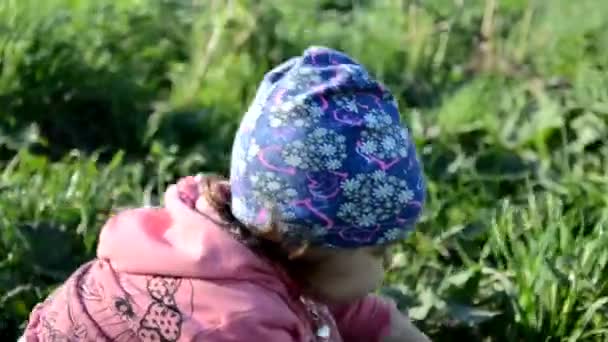 Leende söt lekfull liten flicka står på grönt gräs. Flicka småbarn promenader runt sjön lär sig att gå. solig speing eller sommardag — Stockvideo