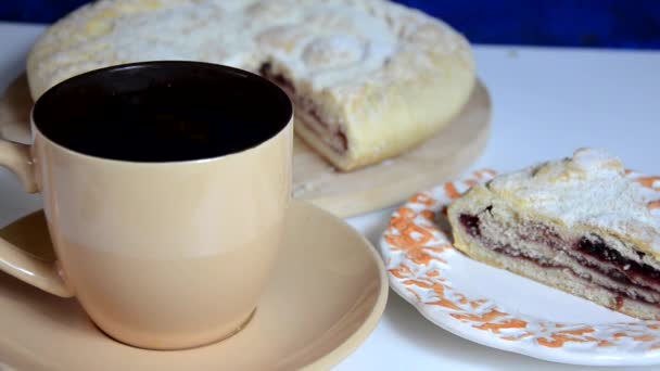 The girl Cuts off and takes a piece of homemade cake, sprinkles icing sugar, pours tea, breakfast or dinner. Homemade pie with cherry berries, cup of tea and fork on white wooden table. Top view. — Stock Video