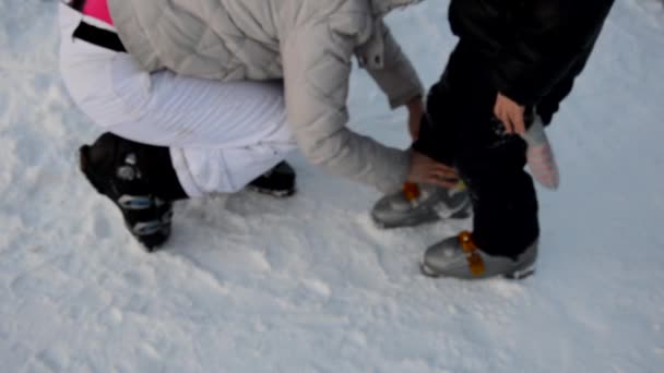 Подготовка к катанию на лыжах - крепление сапог. Мама помогает сыну носить лыжные ботинки. Зимний спорт. открытый. — стоковое видео