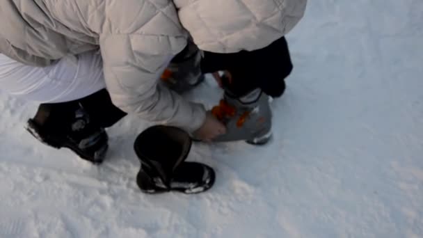 Zich klaarmaken voor het skiën - de laarzen vastmaken. Mam helpt haar zoon om skischoenen te dragen. Wintersport. Buiten. — Stockvideo