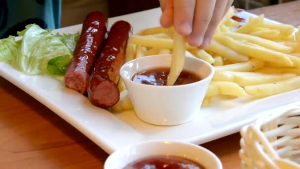 Adolescent într-o cafenea mâncând cartofi prăjiţi, cârnaţi prăjiţi cu ketchup. Satisfăcut, fericit. junk food, fast food. Tineri băiat în interior mănâncă pește și chips-uri zâmbind — Videoclip de stoc