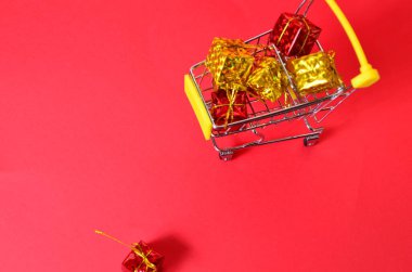 Alışveriş arabasında kurdeleli bir kutu. Konsept - hediye almak. Kırmızı arkaplan konsepti ile ilgili online alışveriş ya da yeni yıl için