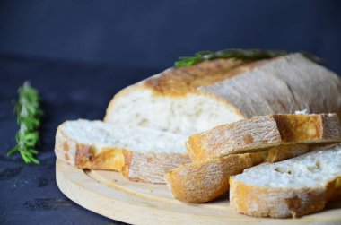 İtalyan ciabatta ekmeği, ahşap kesim tahtasına dilimlenmiş, otlar, sarımsak ve zeytinlerle koyu grunge karşı, üst manzara.