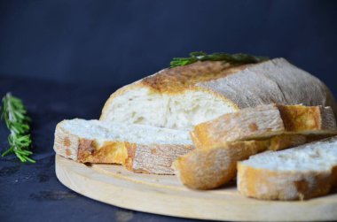 İtalyan ciabatta ekmeği dilimlenmiş tahta kesim tahtasına otlar, biberiye sarımsağı ve koyu grunge arkaplanı üzerine zeytin, üst manzara.