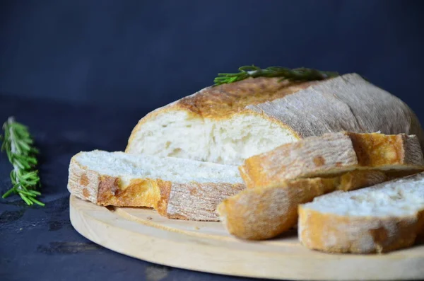 İtalyan ciabatta ekmeği dilimlenmiş tahta kesim tahtasına otlar, biberiye sarımsağı ve koyu grunge arkaplanı üzerine zeytin, üst manzara.