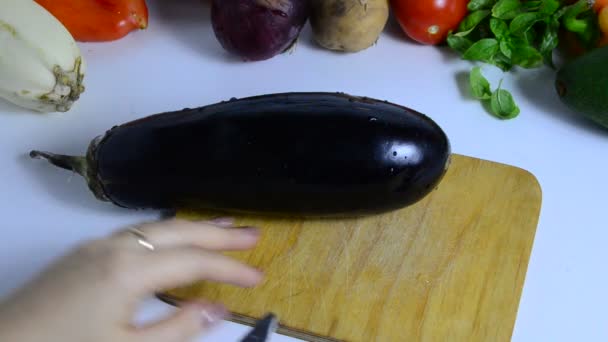 Mão feminina com faca corta berinjela a bordo na cozinha. Cozinhar vegetais. fazer um guisado vegetal ou salada. vegetarianismo, dieta, baixas calorias, nutrição adequada — Vídeo de Stock